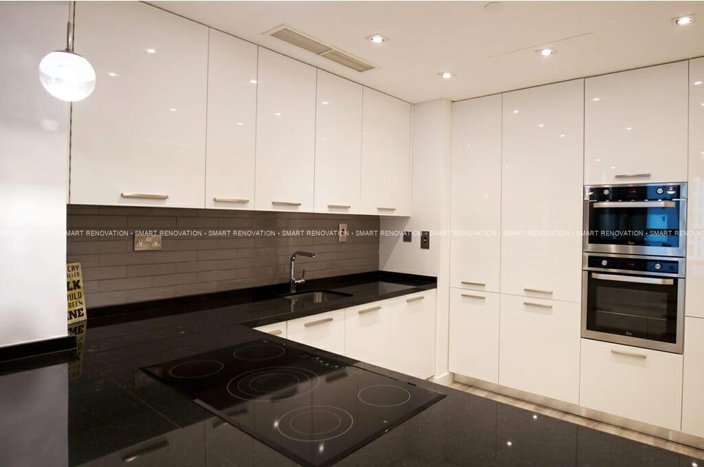 Modern white kitchen with black countertops, dark tile backsplash, induction cooktop, sink, and built-in ovens.